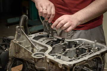 The mechanic repairs the car engine in the workshop, bolts