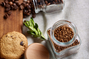Roasted coffee beans get out of overturned glass jar on homespun tablecloth, selective focus, side view