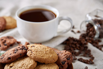 Morning coffee in white cup, chocolate chips cookies on cutting board close-up, selective focus