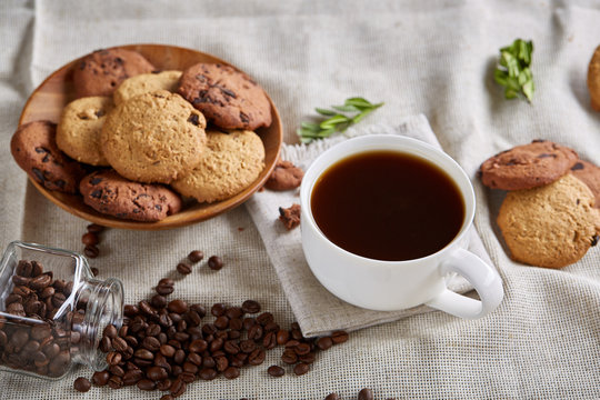 Morning coffee in white cup, chocolate chips cookies on cutting board close-up, selective focus