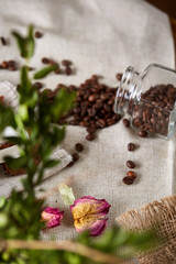 Fototapeta na wymiar Roasted coffee beans get out of overturned glass jar on homespun tablecloth, selective focus, side view
