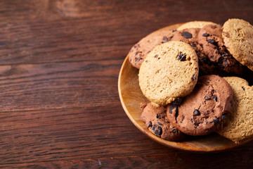 Side view of chocolate chip cookies on a wooden plate over rustic background, selective focus
