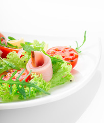 Fresh salad with tomatoes, arugula, cheese and ham on the white plate and white background