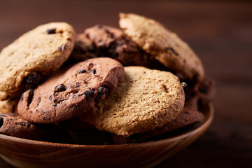 Side view of chocolate chip cookies on a wooden plate over rustic background, selective focus
