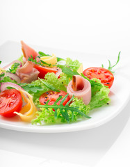 Fresh salad with tomatoes, arugula, cheese and ham on the white plate and white background