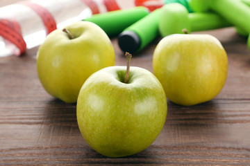 Green apples with skipping rope and dumbbels on brown wooden table