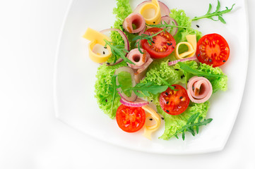 Fresh salad with tomatoes, arugula, cheese and ham on the white plate and white background