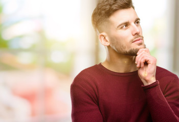 Handsome young man thinking and looking up expressing doubt and wonder