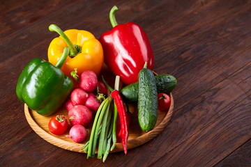 Wooden plate with vegetables for a vegetarian salad on rustic wooden background, close-up, selective focus