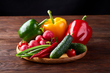 Wooden plate with vegetables for a vegetarian salad on rustic wooden background, close-up, selective focus