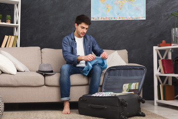 Pensive man packing clothes into travel bag