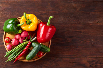 Wooden plate with vegetables for a vegetarian salad on rustic wooden background, close-up, selective focus