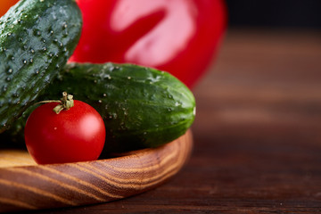 Wooden plate with vegetables for a vegetarian salad on rustic wooden background, close-up, selective focus