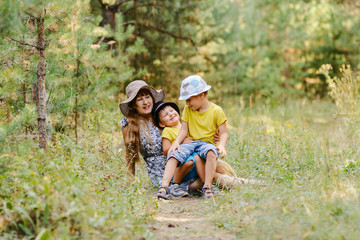 young happy grandmother with two grandchildren sitting on a forest lawn in the summer