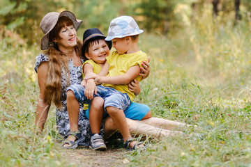 young happy grandmother with two grandchildren sitting on a forest lawn and laughing in the summer