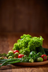 Vegetarian still life of fresh vegetables on wooden plate over rustic background, close-up, flat lay.