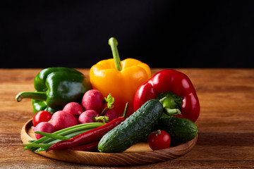 Wooden plate with vegetables for a vegetarian salad on rustic wooden background, close-up, selective focus