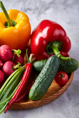 Wooden plate with vegetables for a vegetarian salad on white textured background, close-up, selective focus