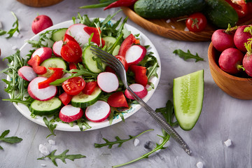 Wooden plate with vegetables for a vegetarian salad on white textured background, close-up, selective focus