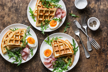Potato savory waffles with boiled egg, ham and arugula on wooden background, top view. Served breakfast, snack, brunch. Flat lay