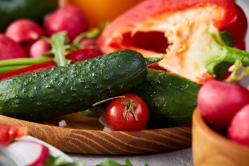 Wooden plate with vegetables for a vegetarian salad on white textured background, close-up, selective focus