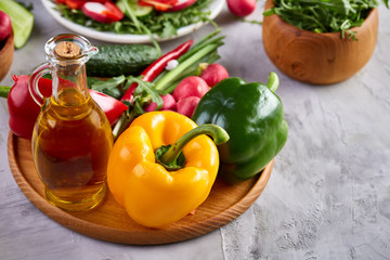 Wooden plate with vegetables for a vegetarian salad on white textured background, close-up, selective focus
