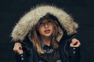 Portrait of a sexy blonde girl in a winter jacket and fleece shirt, standing in a studio.