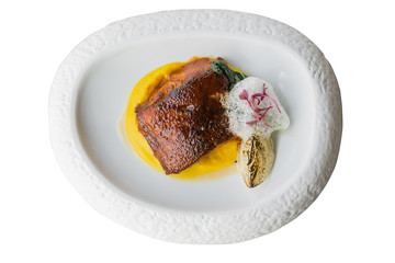 Isolated top view of pan seared trout. served with yellow sauce, foam amd roasted sliced onion on curved white plate. 
