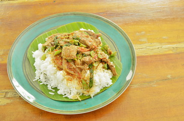 spicy fried duck meat curry with basil leaf and rice on fresh banana leaf