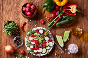 Fresh red radish in wooden bowl among plates with vegetables, herbs and spicies, top view, selective focus.