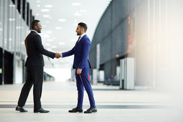 Two young intercultural businessmen greeting one another by handshake in airport lounge after arrival