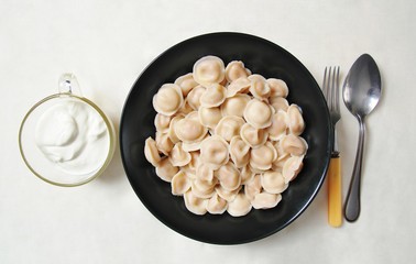 Traditional dish of dumplings in a bowl on a white tablecloth. Served with sour cream, a fork and a spoon.