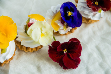 dessert: a set of cakes with cream and edible flowers( Pansy) on a light textile background