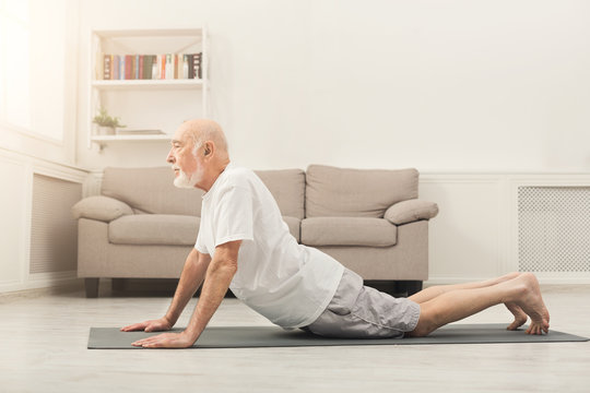 Senior man training yoga in cobra pose indoors