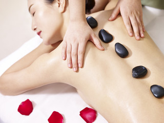 young asian woman receiving hot stone massage in spa salon