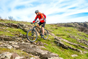 Cyclist in Red Jacket Riding Mountain Bike Down Rocky Hill. Extreme Sport and Adventure Concept.