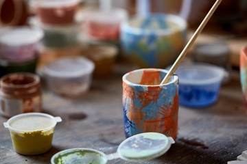 Close-up of various paint mugs and brushes in holder on worktop, selective focus, side view.