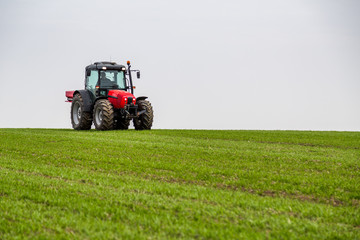 Farmer in tractor fertilizing wheat field at spring with npk