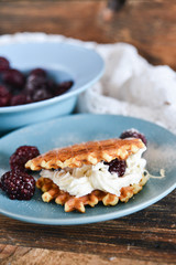 Round waffles with fresh blackberries and whipped cream, on natural wooden background in rustic style