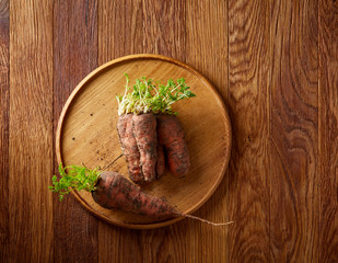 Bundle of carrots with soil over rustic wooden background, side view, close-up, selective focus, low key