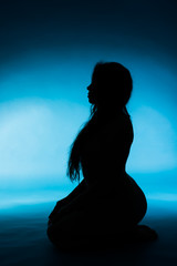 silhouette of nude young woman on blue background