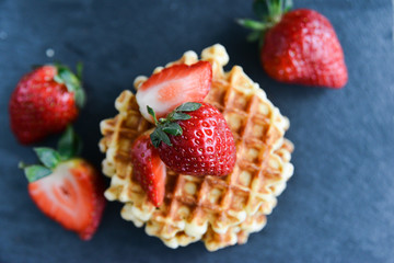 Round waffles with fresh strawberries, on dark background