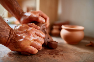 Adult male potter master modeling the clay plate on potter's wheel. Top view, closeup, hands only.