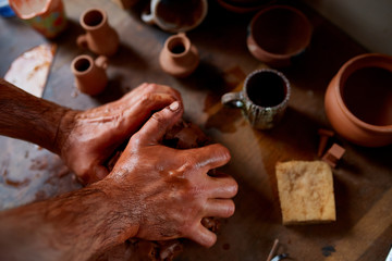 Adult male potter master modeling the clay plate on potter's wheel. Top view, closeup, hands only.