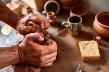 Adult male potter master modeling the clay plate on potter's wheel. Top view, closeup, hands only.