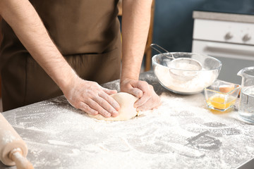 Obraz na płótnie Canvas Man kneading dough on table covered with flour in kitchen