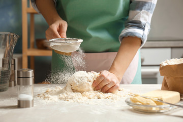Woman sprinkling flour over dough on table in kitchen