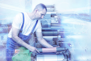 Printer operator next to the printing machine, holding printing cylinder with polymer relief plate stuck on it. Scene showing the preparation for the printing process. Stack press proces