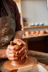 Adult male potter master modeling the clay plate on potter's wheel. Top view, closeup, hands only.