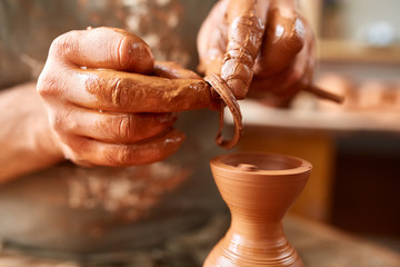 Adult male potter master modeling the clay plate on potter's wheel. Top view, closeup, hands only.